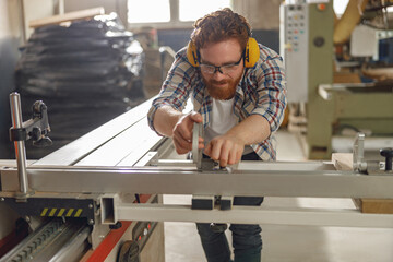 Smiling carpenter cutting wooden board at sawmill carpentry manufacturing and looks camera