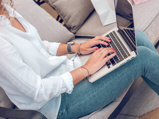 Crop female typing on keyboard of laptop sitting on sofa