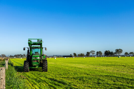 Green tractor in paddock on farm under blue morning sky