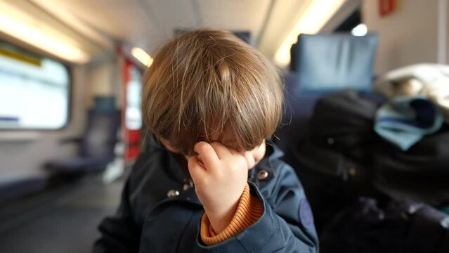 Child rubbing eye with hand while traveling by train. Small boy scratching face taking care of itch