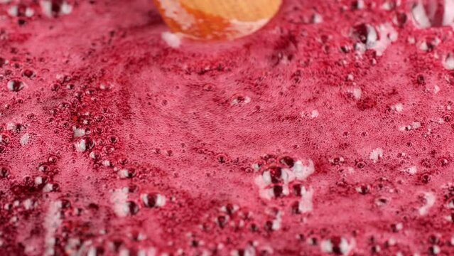 Cooking homemade raspberry jam, close up. Stirring jam with wooden spoon