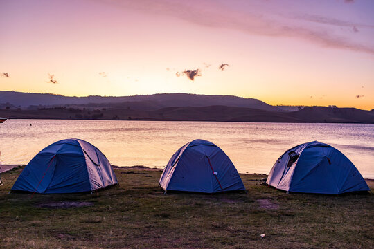 Row of tents at lakeside campground with dusk sky reflecting in lake water