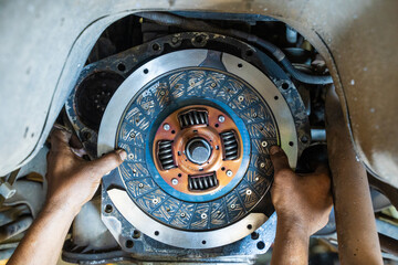 Mechanic's hand installing new clutch plate in car, clutch system, auto mechanic in garage,service...