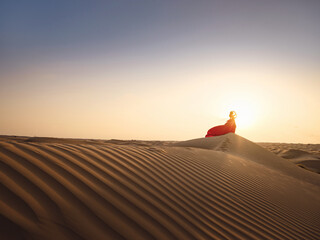 Desert adventure. Young arabian Woman in red silk dress in sands dunes of UAE desert at sunset, fantastic view. The Dubai Desert Conservation Reserve, United Arab Emirates.