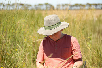 Boy standing in long grass on farm wearing green hat on hot summer day