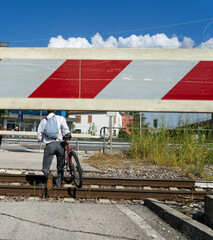 A man with bicycle crosses train tracks while the crossing bar is lowered at a remotely controlled level crossing                      
