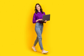 Full body profile photo of cheerful pretty lady use netbook walking empty space isolated on yellow color background