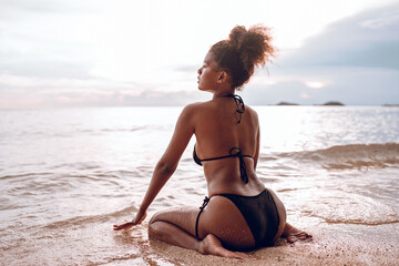 Fototapeta na wymiar Beautiful African american woman in pink bikini on tropical beach. Portrait of dark skinned woman smiling at sea. Brunette tanned girl in swimwear enjoying and walking on beach.