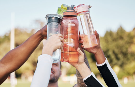 Hands, water bottle and cheers for team sports exercise, fitness or training outdoor on grass field. Diversity sports people, healthy cardio workout and goals in sun as athlete, motivation or support