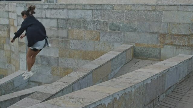 Young active Caucasian woman practicing parkour jumps outdoors in city downtown