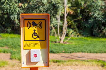 Plate with yellow sign of disabled person in wheelchair and with red button to call staff for help. Translation: Calling. Braille translator: Calling staff under the sign