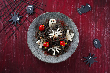 Traditional Halloween octopus spaghetti with Dracula spiders, bats and blood-dripping tomatoes served as top viewin a Nordic design plate with spider web