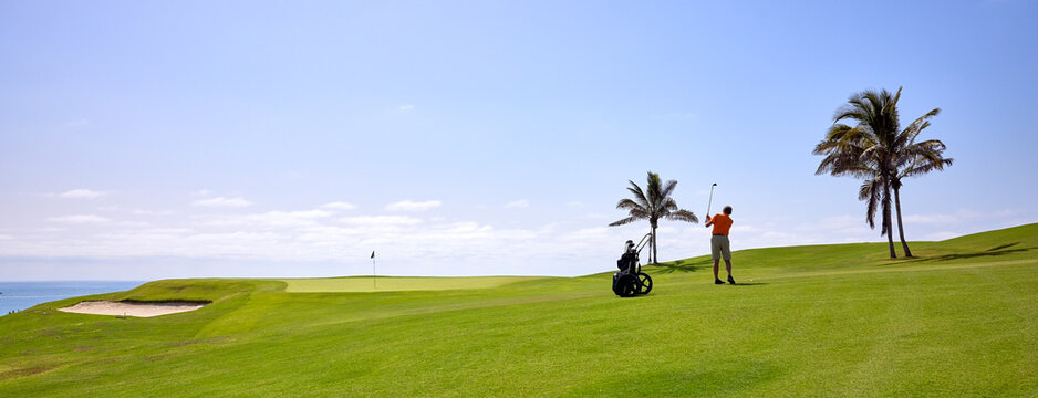 Golfer on a golf course, near the flag on the green. Golfer with golf club hitting the ball for the perfect shot.