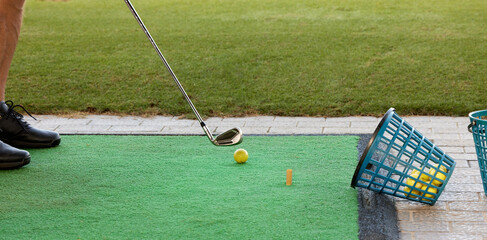 The golfer practices on the driving range with a golf iron and with many balls placed in the basket.