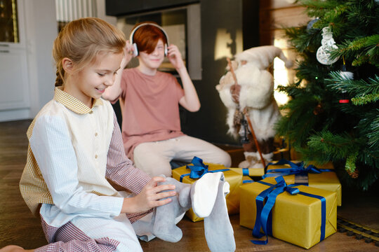 Horizontal shot of boy and his sister wearing pyjamas sitting in front of Christmas tree choosing gift boxes