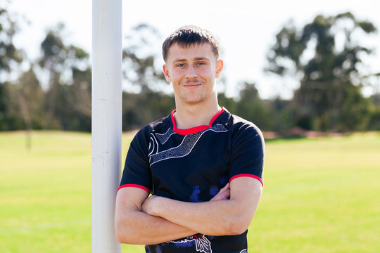 Smiling portrait of first nations sports person with arms folded leaning on goal post