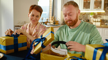 Horizontal shot of joyful Caucasian man and woman sitting at table in kitchen preparing gifts for Christmas together