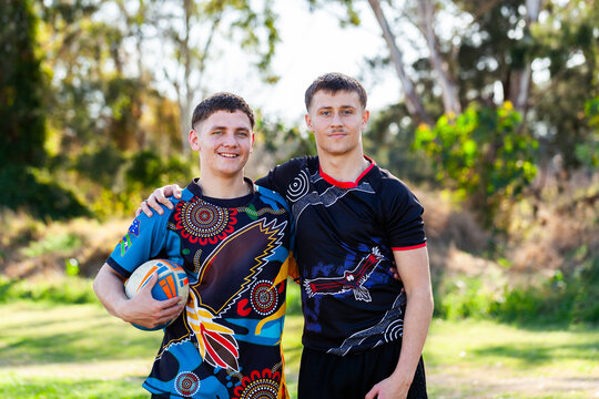 First Nations Australian teammates together on edge of sports area holding football
