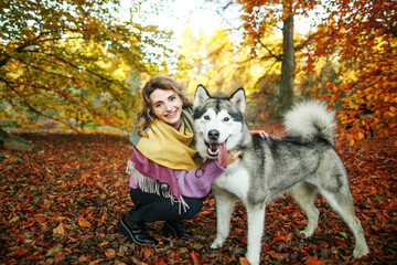Beautiful girl plays with a dog (black and white husky with blue eyes) in autumn park.