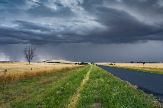 Low angled view of dark storm clouds and rain advancing over a road through a rural setting