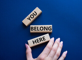 You belong here symbol. Wooden blocks with words You belong here. Beautiful dark blue background. Businessman hand. Business and You belong here concept. Copy space.