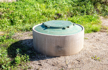 Covered sewer manhole of rural septic tank with green plastic cover. Sanitary sewer system manhole