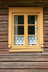 Yellow framed windows on a old weathered wooden building with white traditional lace curtains in the window.