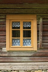 Yellow framed windows on a old weathered wooden building with white traditional lace curtains in the window.