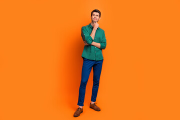 Full length cadre of make decision smart young man wear green shirt touch chin creative idea novelty isolated on orange color background