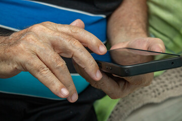 Detalhe das mãos de um homem idoso que está usando um telefone celular.