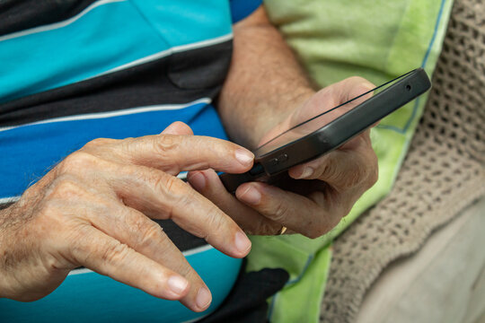 Detalhe das m&atilde;os de um homem idoso que est&aacute; usando um telefone celular.