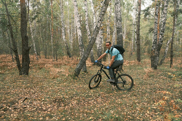 Fototapeta premium man with a backpack and glasses rides a mountain bike in autumn through the forest.An active lifestyle.Cycling