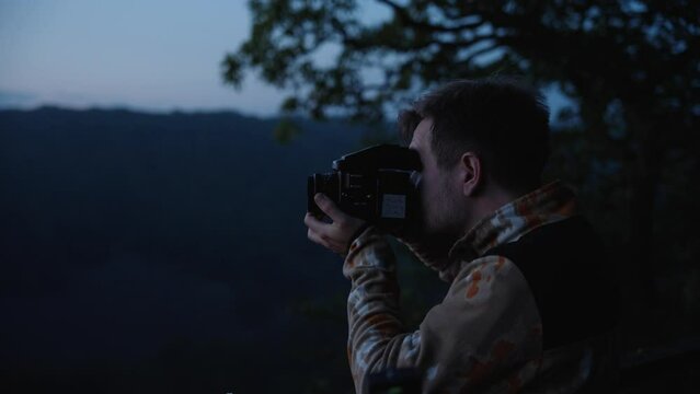 Young man operating a vintage camera in sweden's nature at blue hour dusk. Looking for the perfect composition