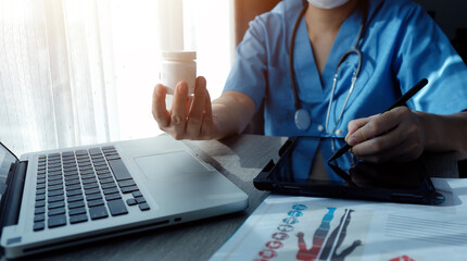 Doctor's working on laptop computer, writing prescription clipboard with record information paper folders on desk in hospital or clinic, Healthcare and medical concept. Focus on stethoscope