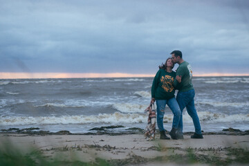 Relationship concept young man and woman in winter clothes walking along stormy sea coast ,