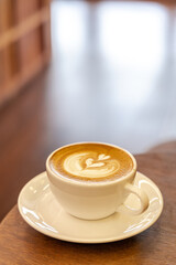 Hot latte coffee in a cup placed on a wooden table in the morning