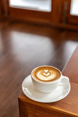 Hot latte coffee in a cup placed on a wooden table in the morning