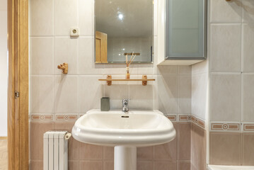 Apartment bathroom with frameless mirror with beveled edges, white cabinet with glass door and white porcelain toilets