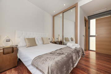 A double bedroom with a sliding-door wardrobe with mirrors, oak wood trim, gold cushions and a white capitone headboard