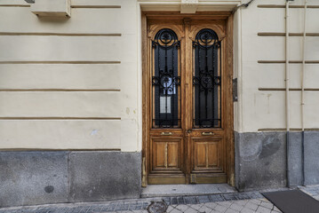 Entrance portal to a building with old wooden doors with black bars with gold details, telephone on a wall and stone steps