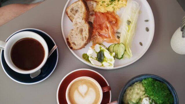 Healthy brunch in the city. Close up of full breakfast, bowl salad with broccoli, avocado. Plate with eggs, salmon and bread, coffee and cappuccino