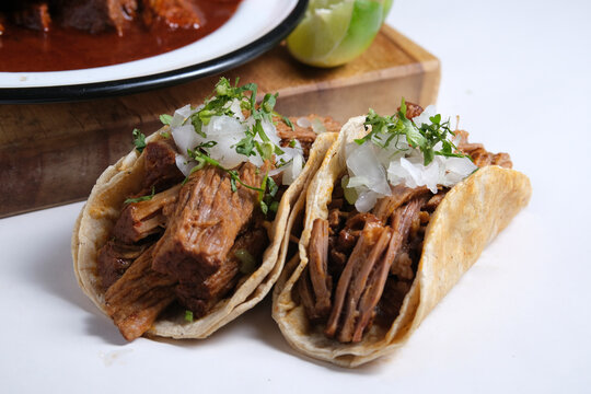 Birria tacos with traditional birria stew plate in background, authentic Mexican food
