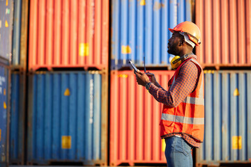African factory worker or engineer using tablet computer and checking work in containers warehouse storage - obrazy, fototapety, plakaty
