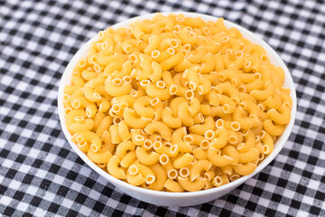 Uncooked Chifferi Rigati Pasta in White Cup on Black Checkered Towel. Fat and Unhealthy Food. Classic Dry Macaroni. Italian Culture and Cuisine. Raw Pasta