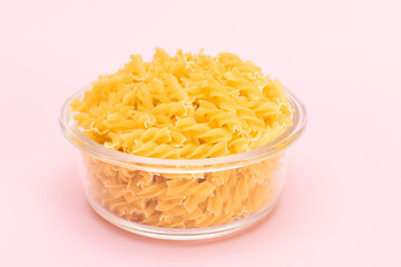Uncooked Fusilli Pasta in Glass Jar on Pink Background. Fat and Unhealthy Food. Classic Dry Spiral Macaroni. Italian Culture and Cuisine. Raw Pasta
