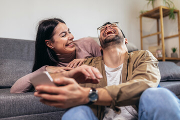 Beautiful young loving couple bonding to each other and making selfie while sitting on the couch together