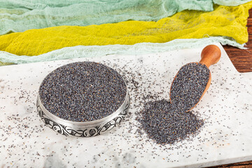 Poppy seeds. Poppy seeds dish with dark fluff in wooden ladle or spoon isolated on marble...