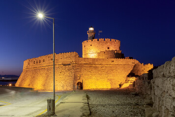 Old stone lighthouse, Saint Nicholas Fort illuminated at night in Rhodes.