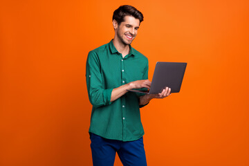 Photo of cute cheerful man dressed green shirt texting apple samsung modern device isolated orange...