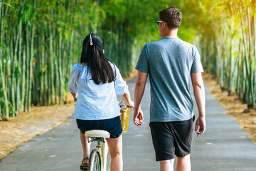 Happy Asian couple enjoy with bicycle in bamboo park. Asian lovers ride bicycle with having fun to...